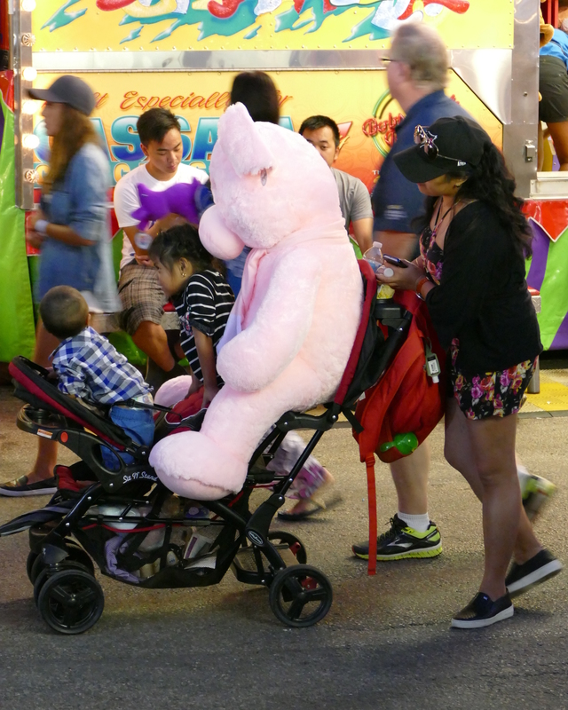 Huge pink stuffed toy shares a stroller with a couple kids.