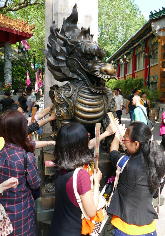 Several people all trying to touch a brass dragon at the entrance to Sik Sik Yuen Temple