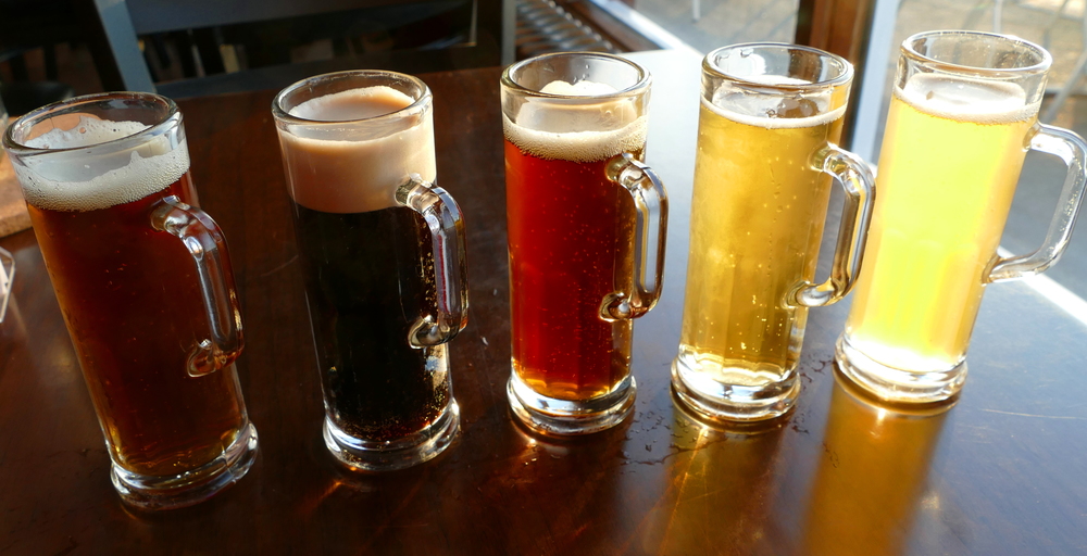 five small beer samples of different colours in miniature tall mugs
