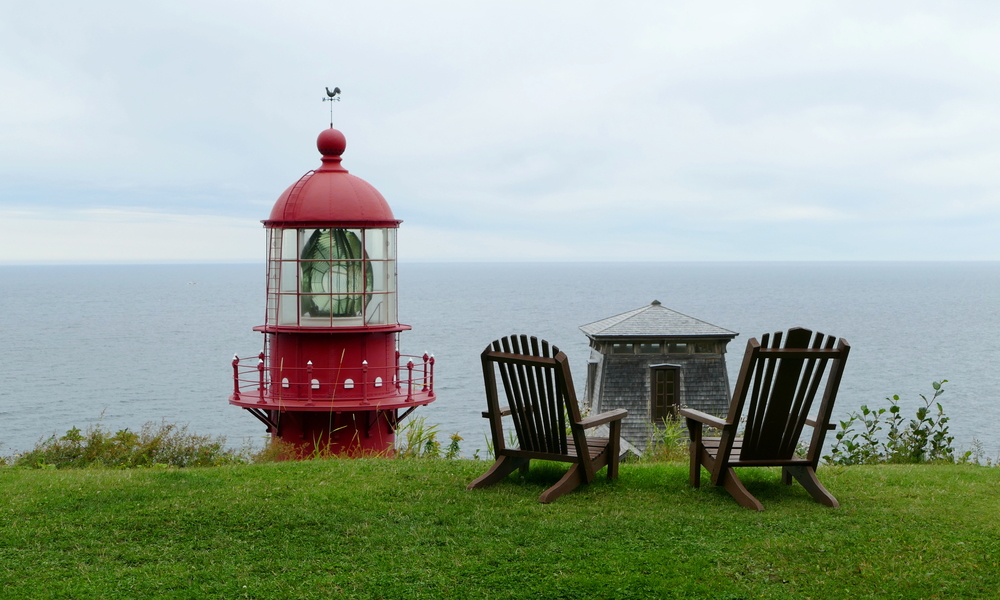 The top of a lighthouse over a hill beside two deck chairs