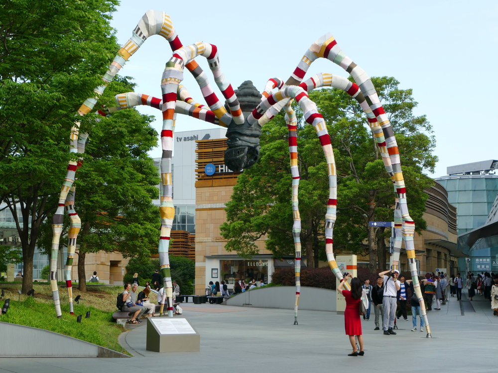 a very large spider-like sculpture, now with multi-coloured fabric leggings in the middle of an outdoor mall