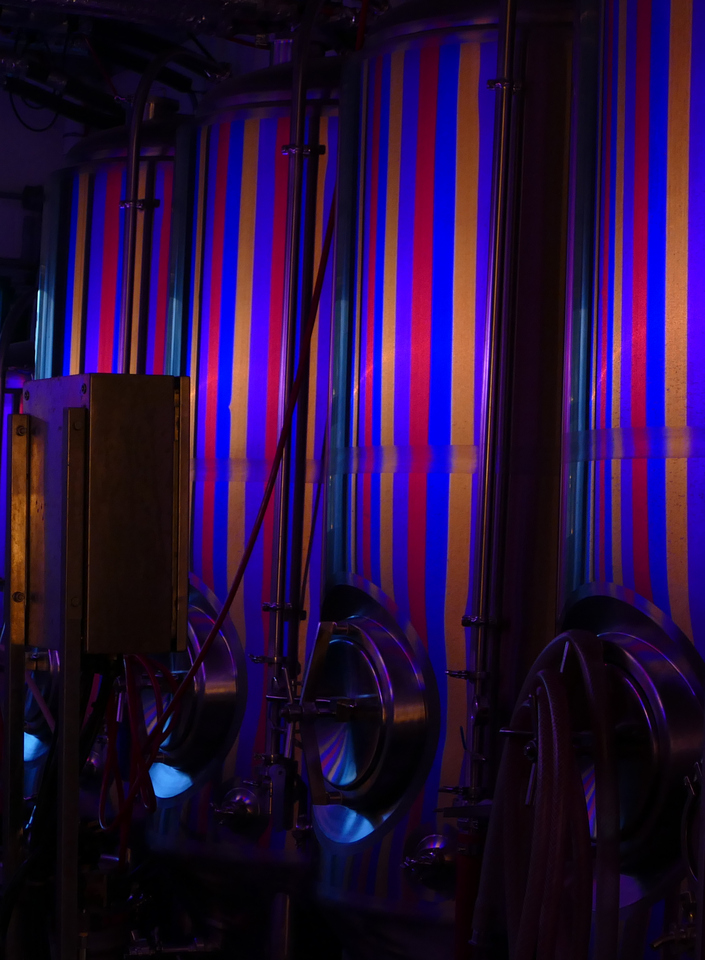 Coloured stripes of light reflecting off several large stainless steel tanks.