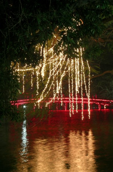 Red-lit bridge over the lake with streaming lights hanging down.