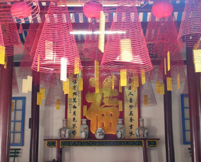 Lots of expanding spirals of red incense hanging from the ceiling of a temple.