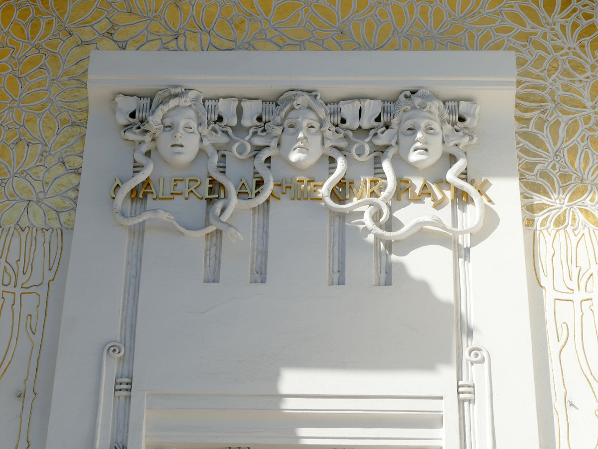 three very white sculpted faces with snake hair surrounded by gold leaf