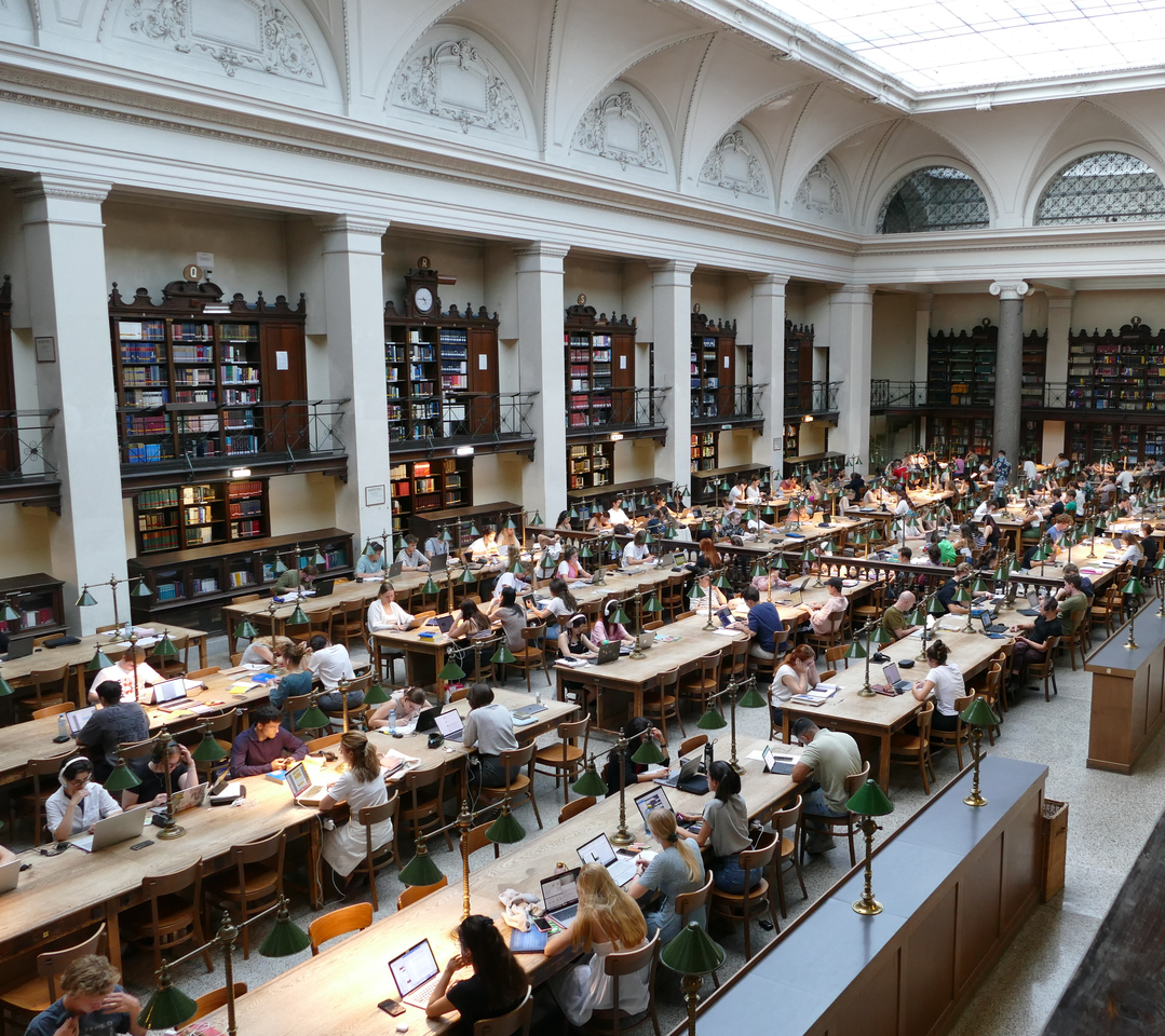 rows of tables with banker's lights and students studying surrounded by arcade shelving