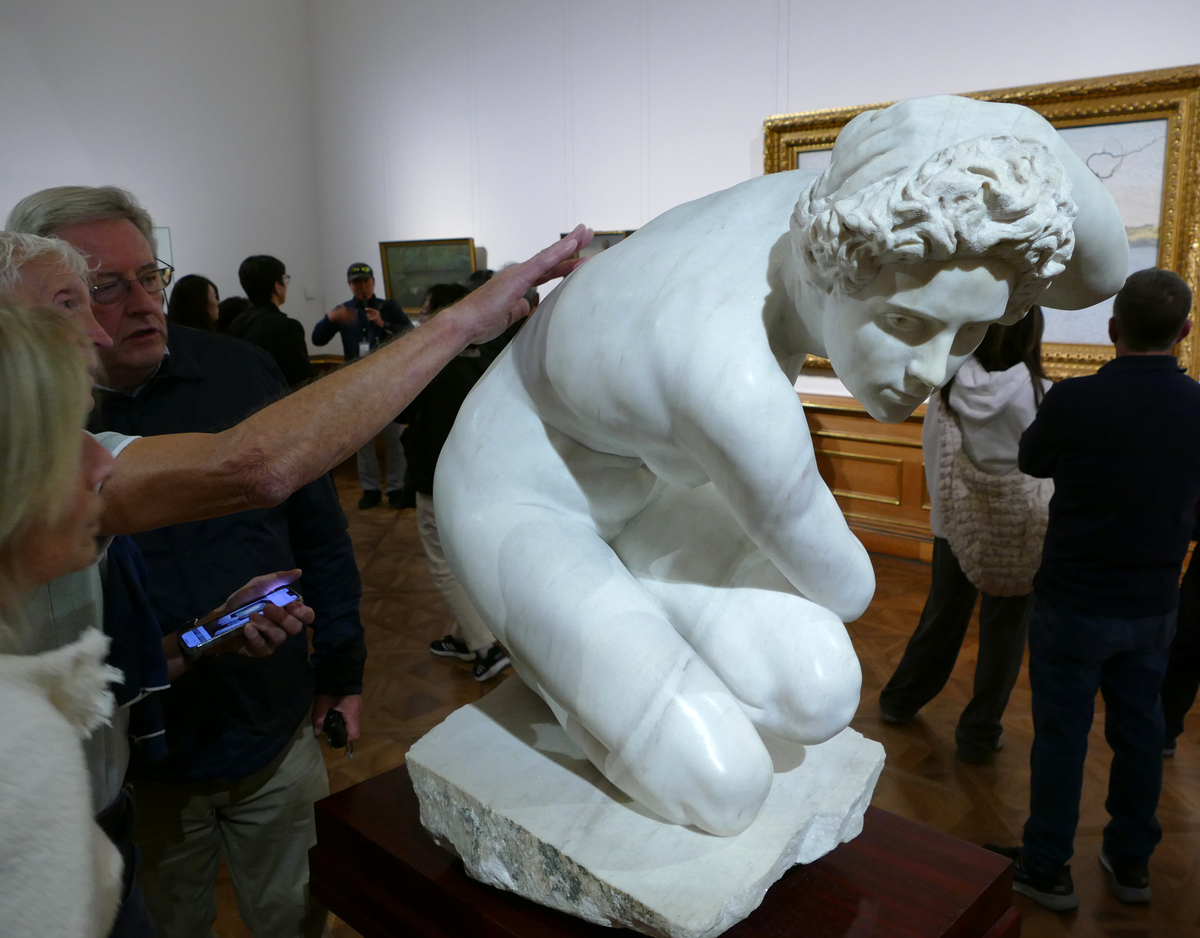 A woman runs her fingers down the back of a sculpture of a crouching woman